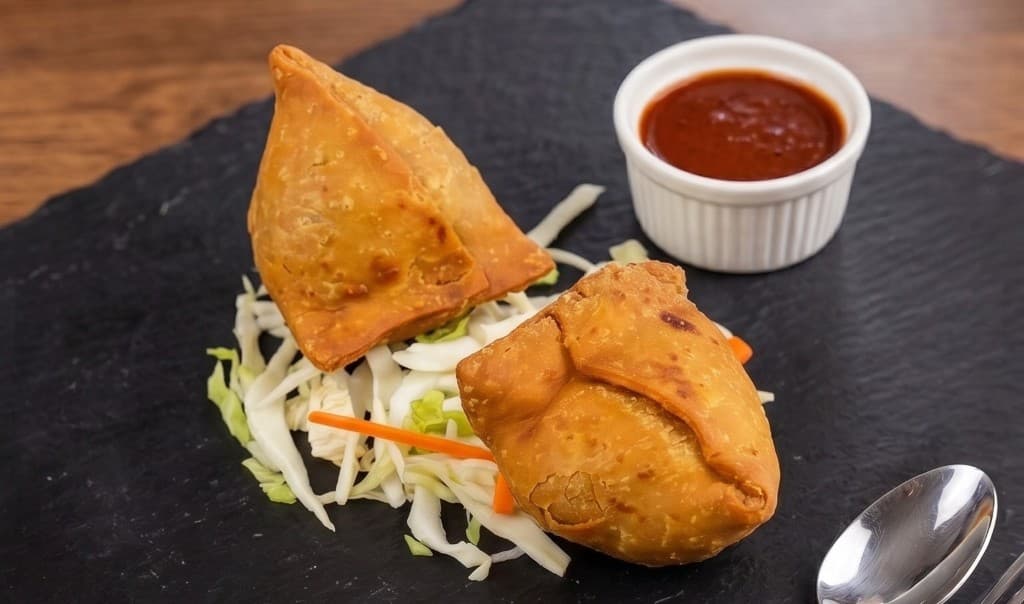 Punjabi Veg Samosa, golden crispy pastry with tamarind chutney on a slate platter